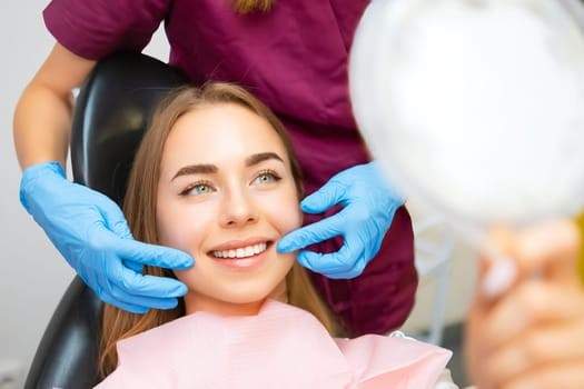 patient in a dental chair with technician wearing blue gloves pulling both sides of her cheeks into a smile