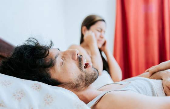 A  man snoring in bed and wife covering her ears